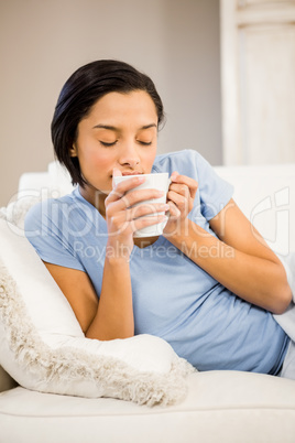 Peaceful brunette drinking by white cup