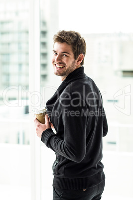 Handsome man holding disposable cup looking back to camera