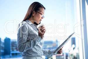 Smiling businesswoman holding disposable cup reading newspaper