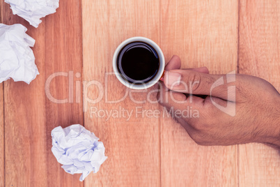 Hand holding coffee cup by crumbled paper on desk