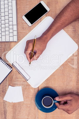 Businessman writing on notebook at desk while holding coffee