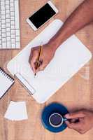 Businessman writing on notebook at desk while holding coffee