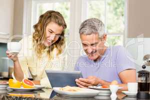 Happy couple using tablet and having breakfast