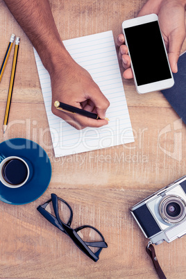 Businessman writing on notepad while holding smart phone