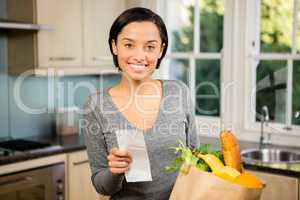 Smiling brunette holding receipt in kitchen
