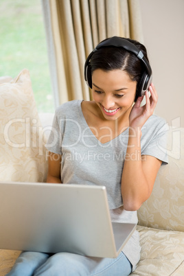 Smiling brunette using laptop and headphones