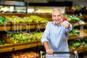 Smiling mature man with thumbs up holding cart