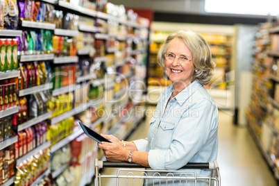 Smiling senior woman with cart using tablet