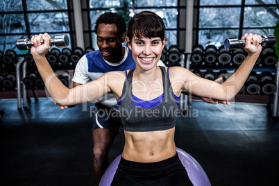 Male trainer helping woman during dumbbells exercise