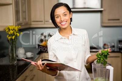 Smiling brunette reading book and preparing smoothie