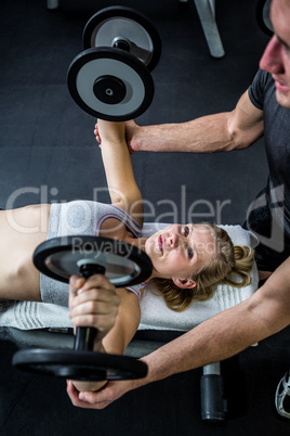 Fit woman doing dumbbells exercise with trainer