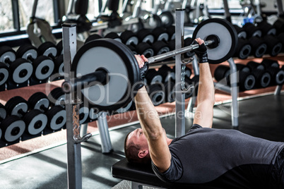 Muscular man lifting barebell while lying on bench