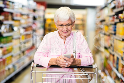 Senior woman using phone while pushing cart