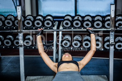 Fit woman lifting barbell while lying on bench