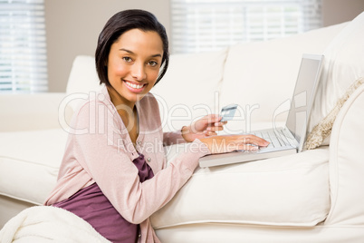 Smiling brunette using laptop and holding credit card