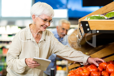 Smiling senior woman with list buying apple