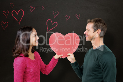 Composite image of smiling couple holding red heart shape