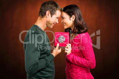 Composite image of cheerful couple holding gift box