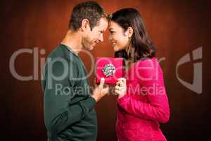 Composite image of cheerful couple holding gift box