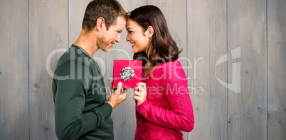 Composite image of cheerful couple holding gift box