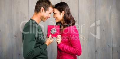 Composite image of cheerful couple holding gift box