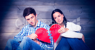 Composite image of young couple sitting on floor with broken hea