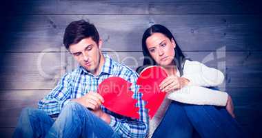 Composite image of young couple sitting on floor with broken hea