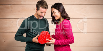 Composite image of happy young couple with heart shape gift