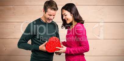 Composite image of happy young couple with heart shape gift