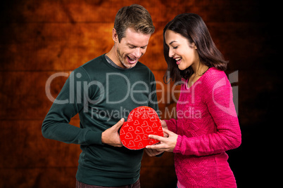 Composite image of happy young couple with heart shape gift