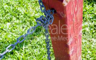 Red fence post with tied metal chain against grass