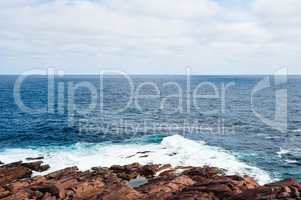 Water and waves splashing on rocky ocean coast under cloudy sky