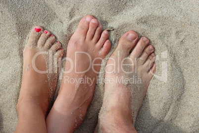 feet of father mother and their daughter on the sand