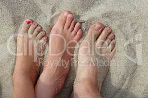 feet of father mother and their daughter on the sand
