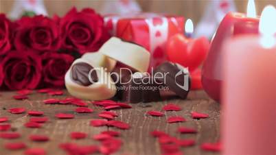 Red roses and chocolate candies with candles on wood