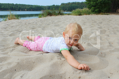 baby lays on the white sand at the river