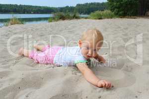 baby lays on the white sand at the river