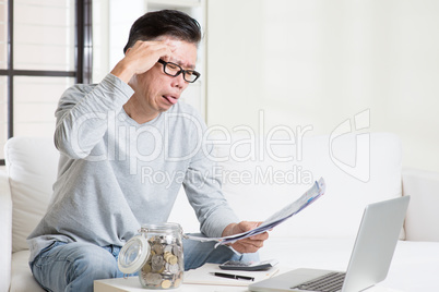Stressed mature Asian man paying bill at home.