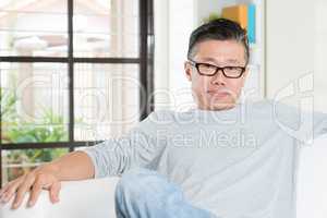 Mature 50s Asian man sitting at home.