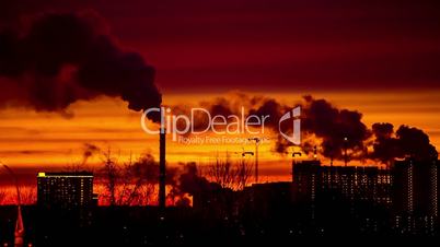 Modern city in the evening at sunset. Smoke comes out of the pipes of power plants and factories of the modern neighborhood on the outskirts of the metropolis. Urbanization.