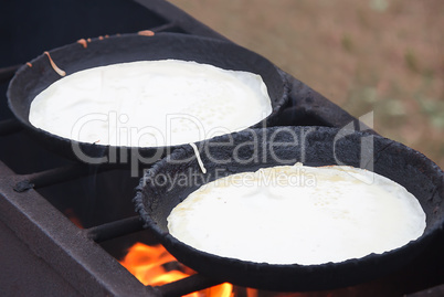 The grill and two frying pans, on them are fried pancakes.