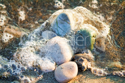 Small sea stones on the seashore, covered with a sea wave.