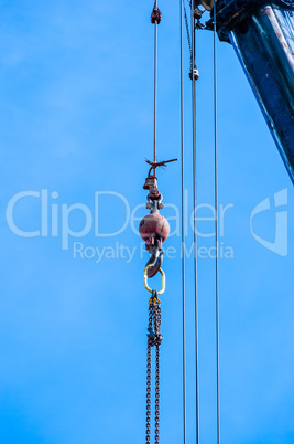 Weight with hook and chain hanging from crane on blue sky