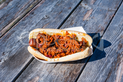 Hot dog covered in chili on wood table