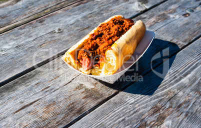 Partly eaten hot dog covered in chili on wood table