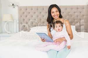 Smiling brunette holding her baby and using tablet