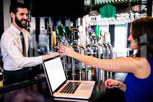Barman giving a drink to customer using laptop
