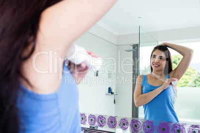 Smiling brunette putting deodorant on her armpit