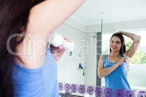 Smiling brunette putting deodorant on her armpit