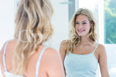 Smiling beautiful young woman looking at herself in the bathroom